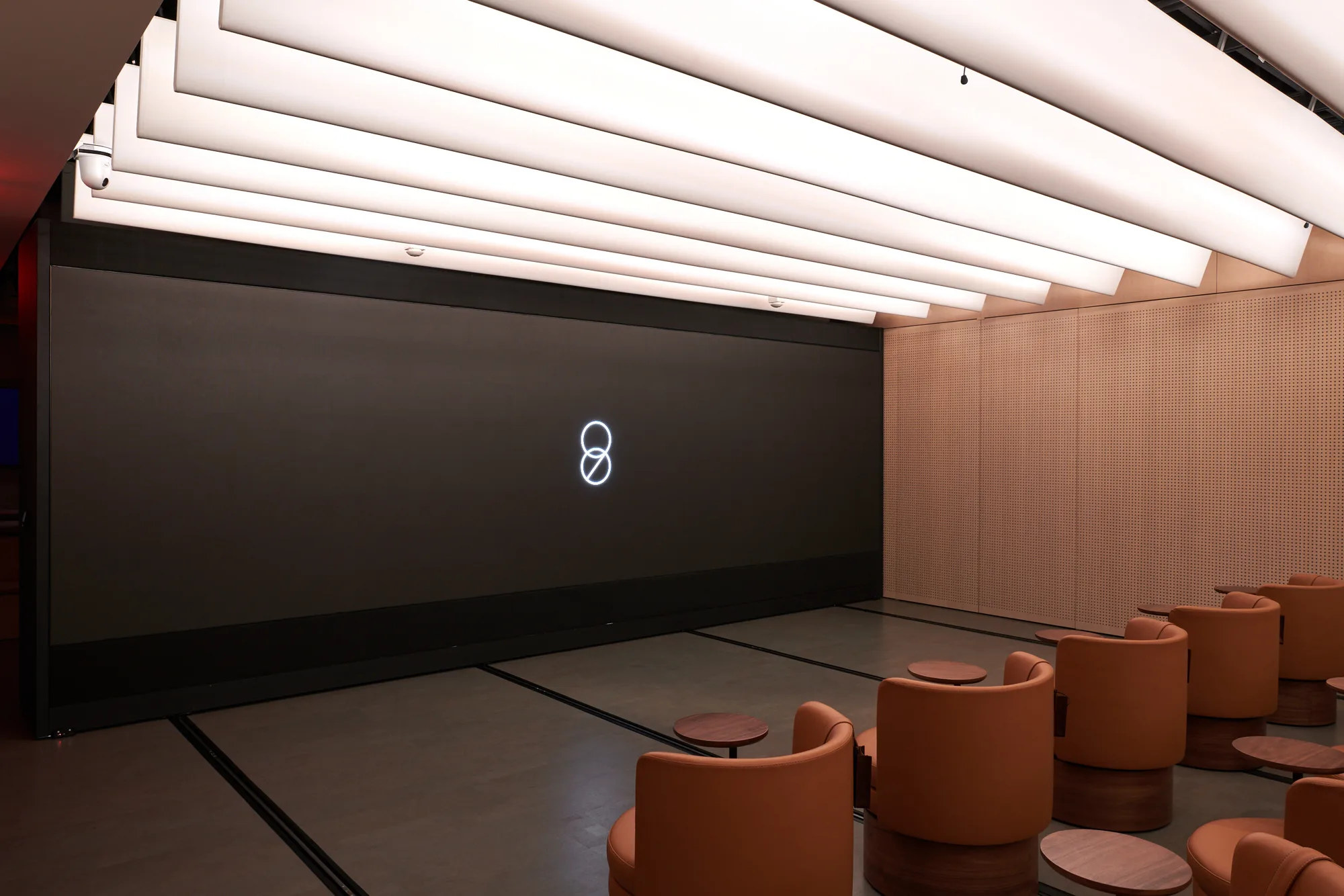 The Presentation Room with a large dark screen showing the Room 98 mark, ringed by timber panels and tan swivel seats.
