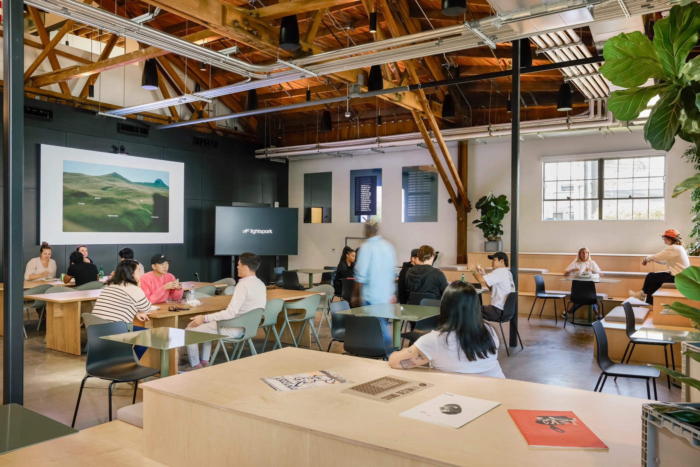 Open-plan workplace with exposed timber trusses, a large landscape artwork on the wall, and people at tables.