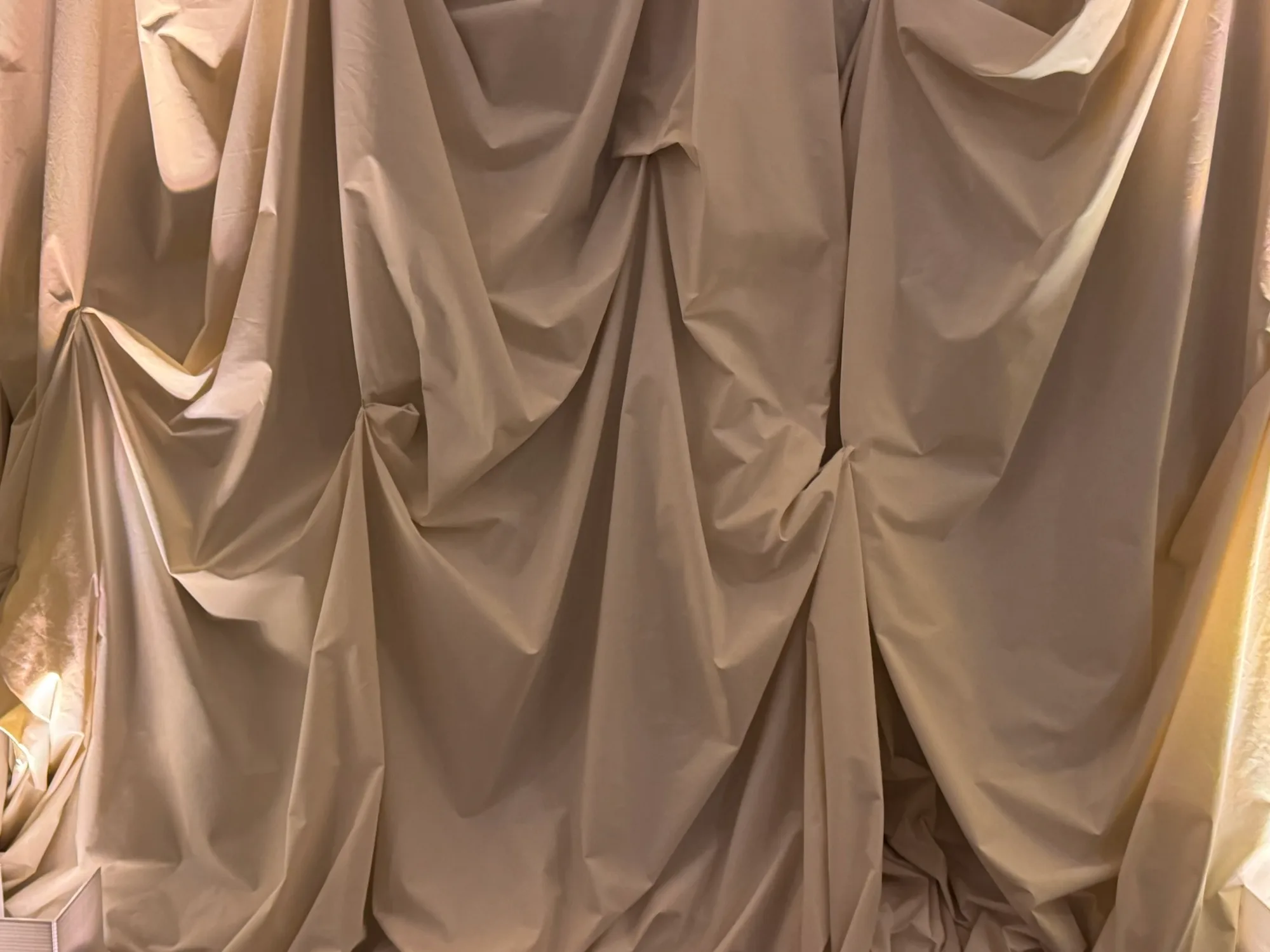 Folds of cream fabric draped over a wall in warm light.