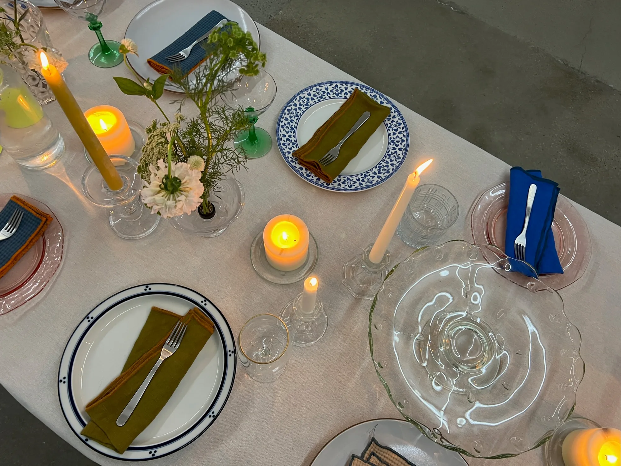 Overhead view of place settings with blue-patterned plates, olive napkins, candles, and green stemware.